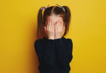 10 tips om kinderen aan het praten te krijgen Verlegen meisje met handen voor gezicht.