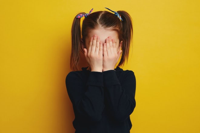 10 tips om kinderen aan het praten te krijgen Verlegen meisje met handen voor gezicht.