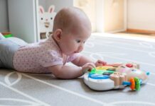 Baby ligt op buik in kinderopvanglocatie met speelgoed voor zich.