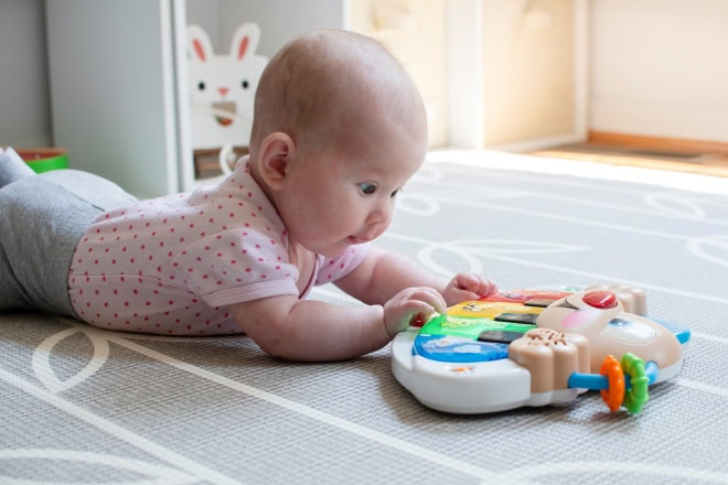 Zó werkt het kinderbrein Baby ligt op buik in kinderopvanglocatie met speelgoed voor zich.