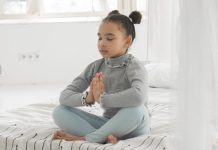 Jong meisje zit met gevouwen handen te mediteren op een kussen.