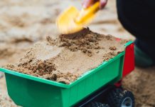 Kind schept zand in zandbak in groene kiepwagen.