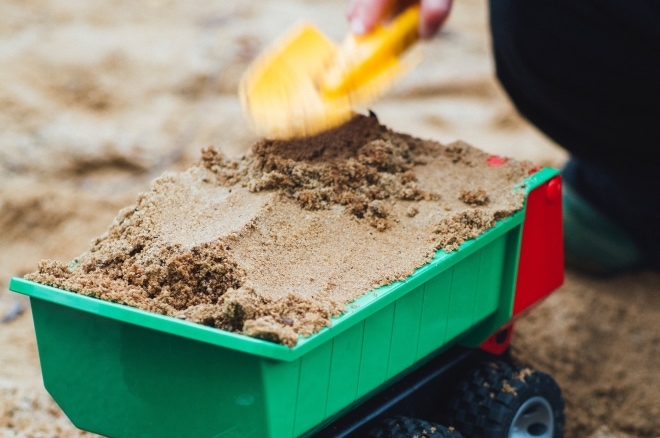 Kind schept zand in zandbak in groene kiepwagen.