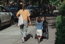 Moeder loopt met dochter en kinderwagen over straat.