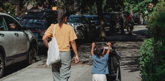 Moeder loopt met dochter en kinderwagen over straat.