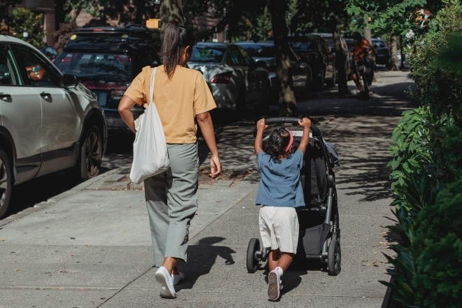 Moeder loopt met dochter en kinderwagen over straat.