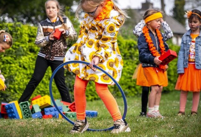 Meisjes spelen op koningsdag in oranje kleding met een hoepel en blokken