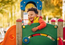 Adorable little 1-2 year old toddler boy having fun on playground, child wearing orange hoody jacket and yellow vest