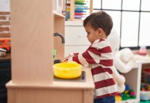 Adorable toddler playing with play kitchen standing at kindergarten