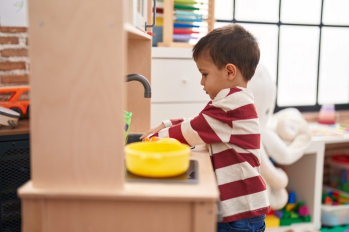 Adorable toddler playing with play kitchen standing at kindergarten
