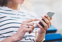 Vrouw zit op blauw bankje en tikt met vinger op smartphone