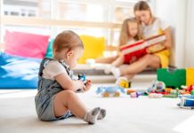 Baby playing with toys while mother and daughter reading book on background, family time, education