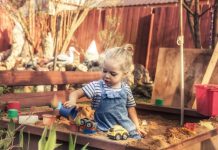 Happy beautiful child girl playing alone outdoors on playground with toy cars in sandbox in countryside concept for childhood lifestyle