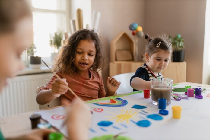 Happy little girls painting picture during creative art and craft class at school.