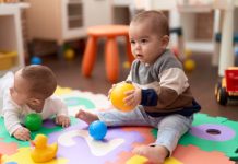 Twee baby's spelen op een kleed met een bal