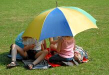 Kinderen die op een grasveld zitten, onder een paraplu tegen de zon.