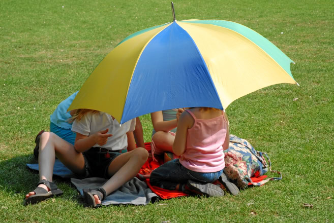 Kinderen die op een grasveld zitten, onder een paraplu tegen de zon.