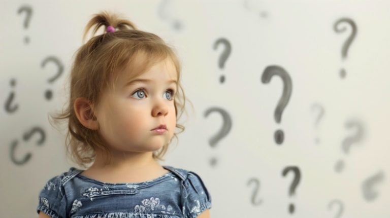 Cute little toddler girl with curious and thoughtful face expression, standing in the room in front of the wall full of question mark symbol drawings, wondering concept, child learning and education