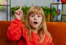 Kind steekt vinger in de lucht en stelt een vraag, jong meisje met pony en rood haar.