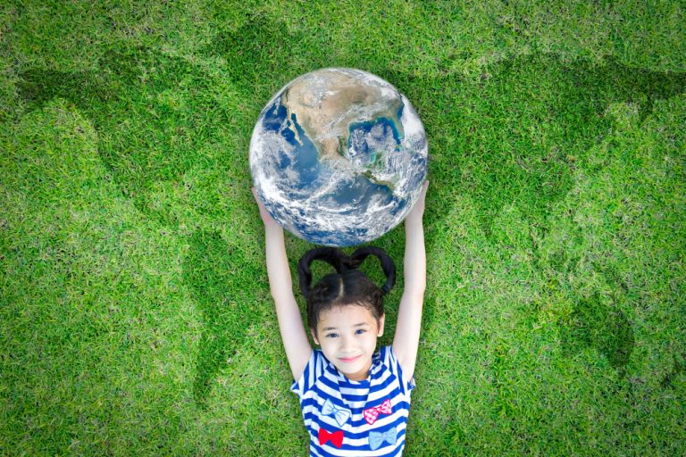 ‘We moéten ons druk maken om een sociale en ecologische wereld voor onze kinderen’ Meisje ligt op een groen tapijt en houdt een aardbol boven haar hoofd vast