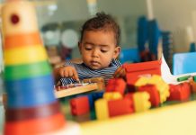 Happy baby playing with toy blocks in the kindergarten.