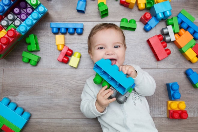 Speelgoed niet altijd vrij van gif, ook als het uit Europa komt Little baby playing with lots of colorful plastic blocks constructor on floor in the room.