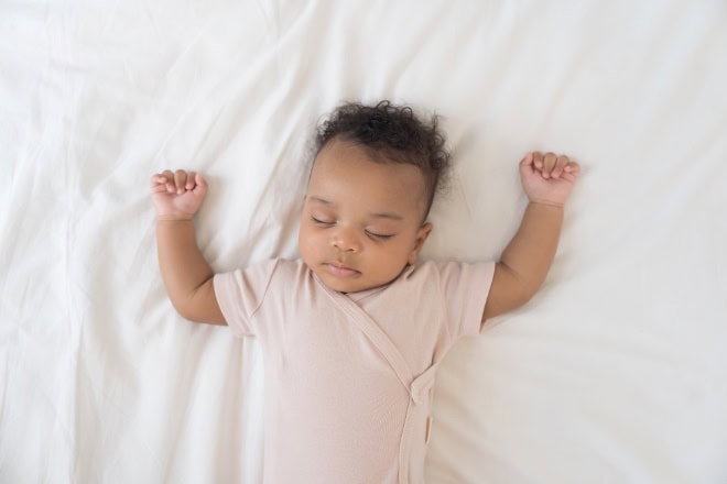 AdobeStock_1674367889-2 Newborn health care. Top view of newborn baby sleeping on white blanket. African American newborn baby sleeping. Newborn baby in diaper lying on bed
