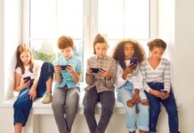 ‘Behandel telefoon als roken: nooit in het bijzijn van kinderen’ Children sitting on windowsill, playing online games on mobile phones and ignoring each other