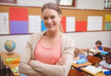 Pretty teacher smiling at camera with arms crossed at the elementary school