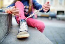 Cute little girl learning to tie shoelaces outdoors on summer day