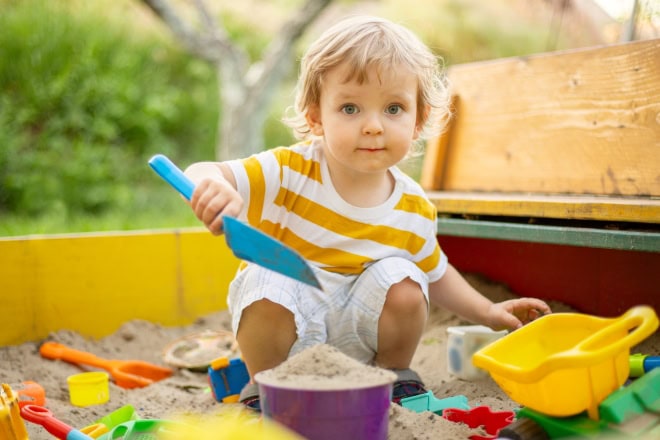 AdobeStock_479399075kl Peuter speelt in zandbak met gekleurd, plastic speelgoed.