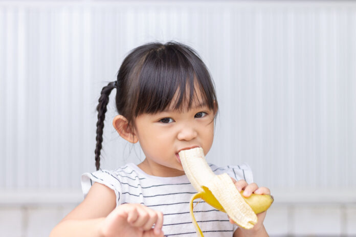 Portrait image of baby 3-4 years old. Happy Asian child girl enjoy eating a banana with sweet smiling. Food and healthy kids concept. Meisje met banaan